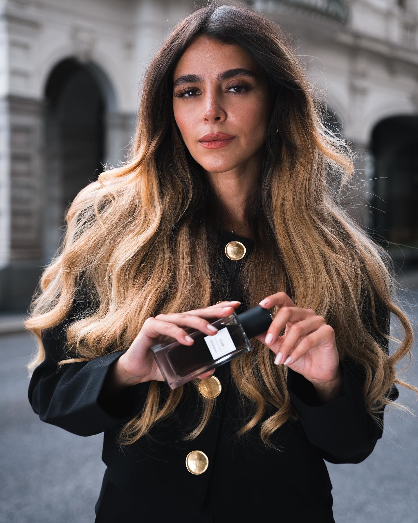 @hilal.yetisti with long ombre hair holding a YSL Cuir fragrance