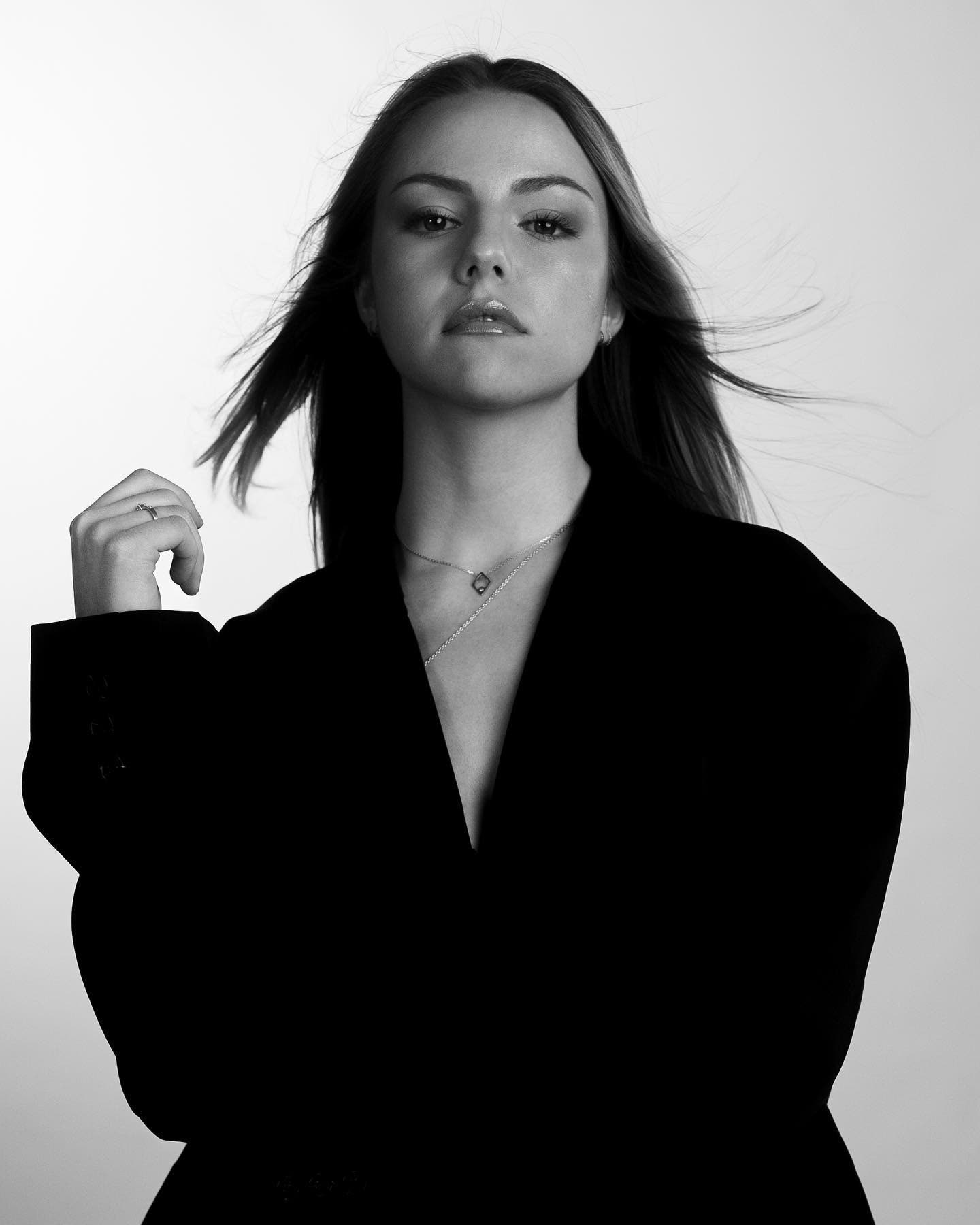 Black-and-white studio portrait of @julia.hhlrr in a black blazer, hair in motion