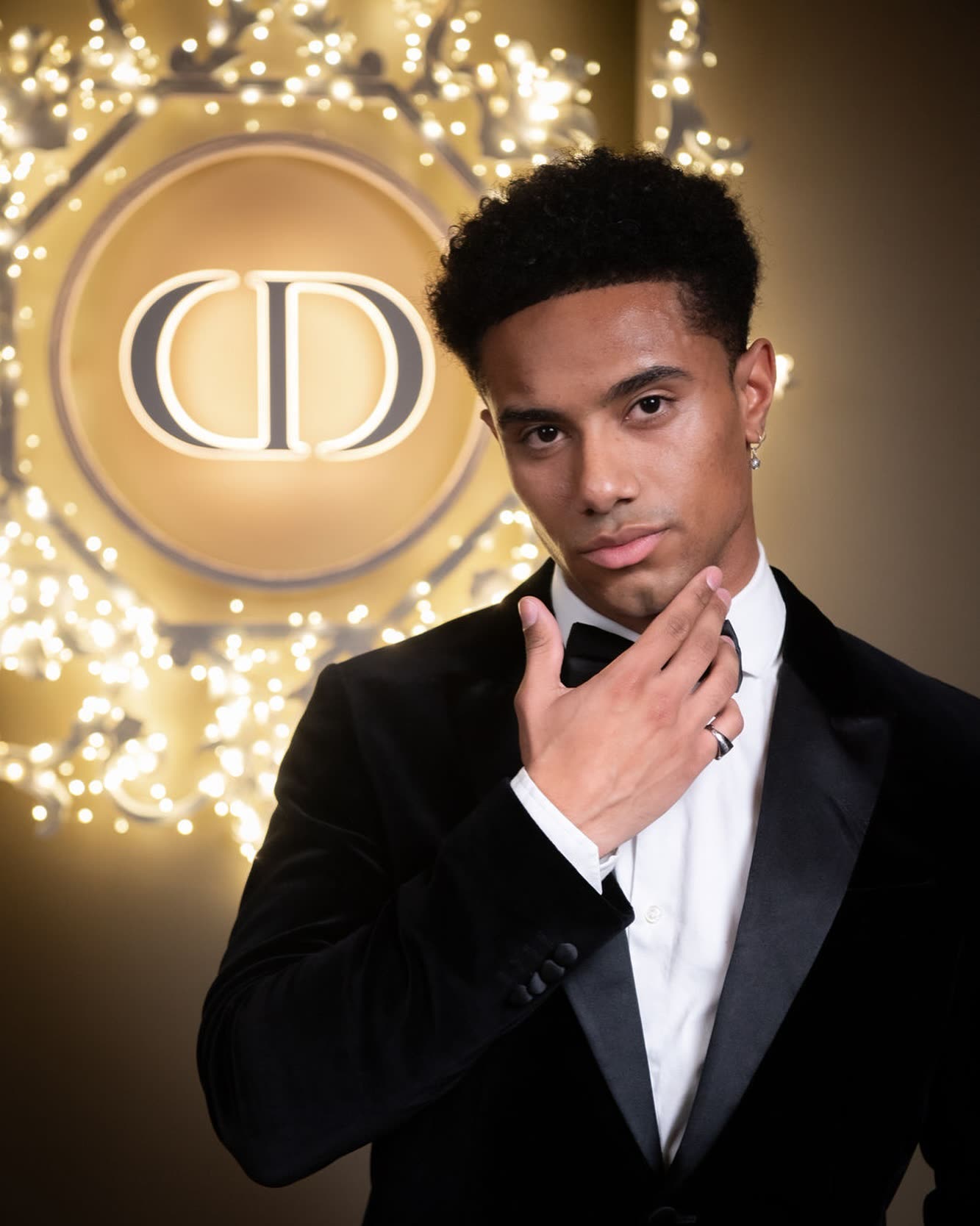@naswyn in a velvet tuxedo before the glowing Dior emblem
