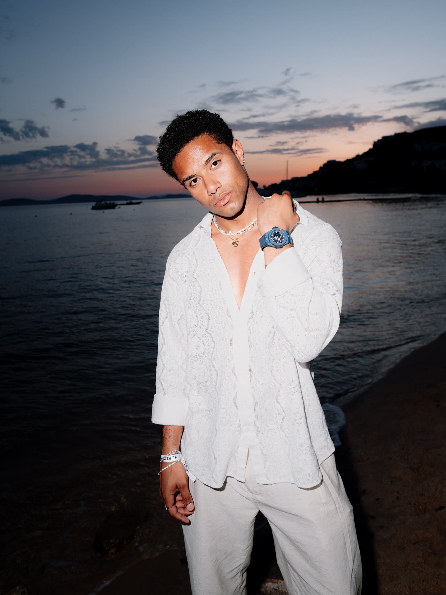 @naswyn in a white lace shirt at a dusk beach wearing a Hublot watch