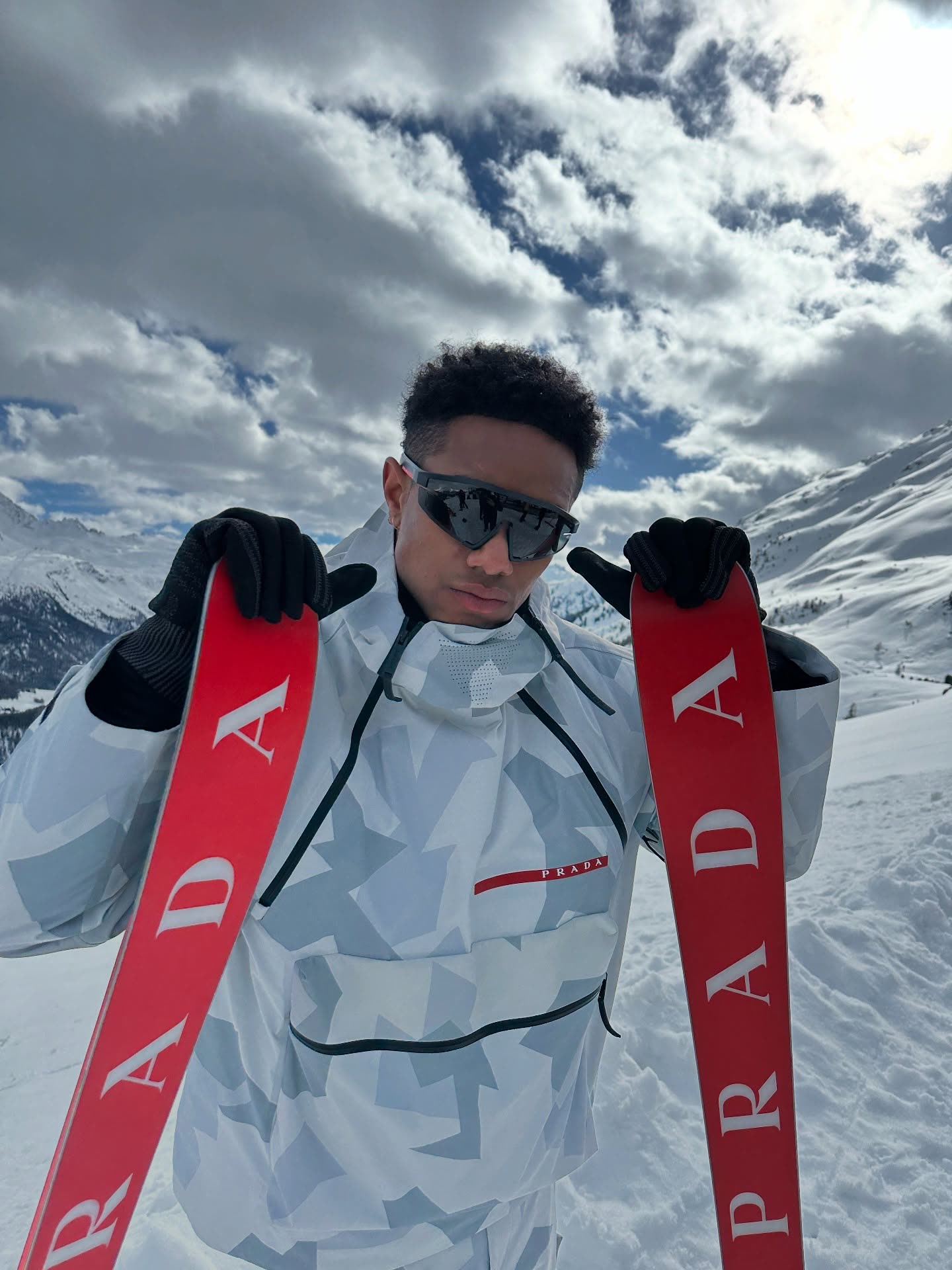 @naswyn on a snowy slope holding red Prada Linea Rossa skis